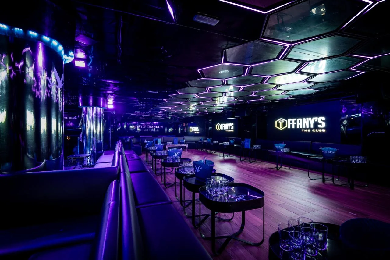Inside Tiffany's The Club — a hexagon-lit ceiling and illuminated 'Tiffany's The Club' signage over banquettes and cocktail tables in purple light