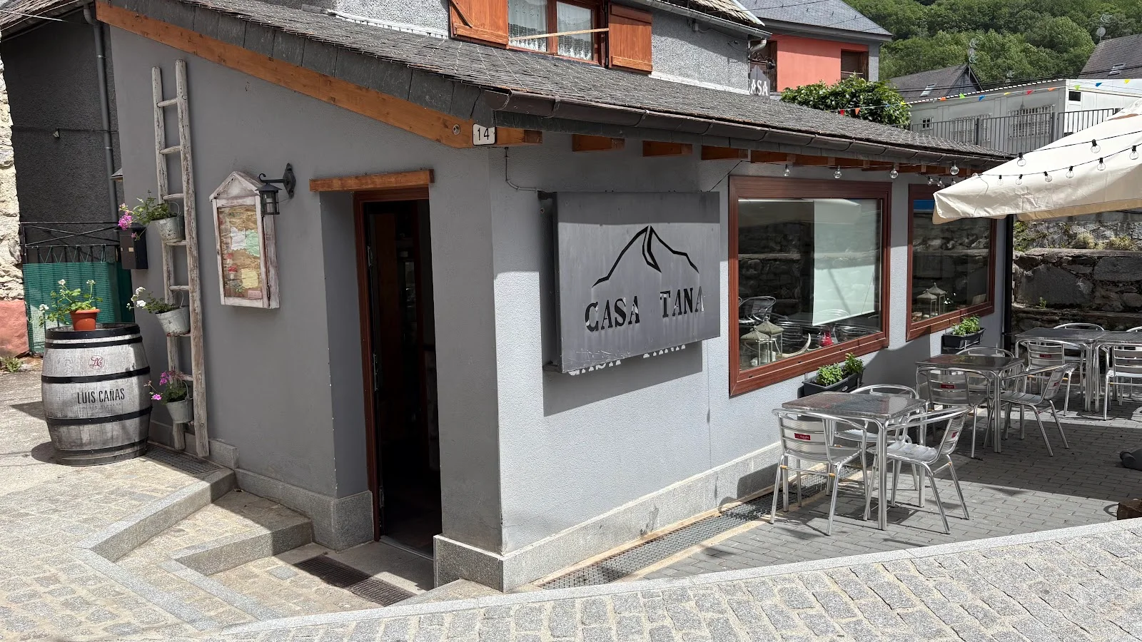 The grey stone facade and mountain-logo sign of Casa Tana on a street in Arties, with a terrace alongside