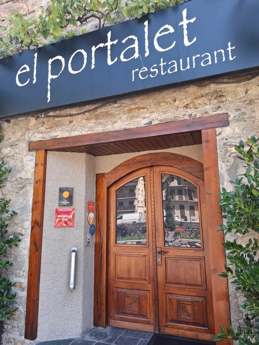 The stone entrance of El Portalet in Bossòst under its black sign, with a Michelin plaque beside the arched wooden doors