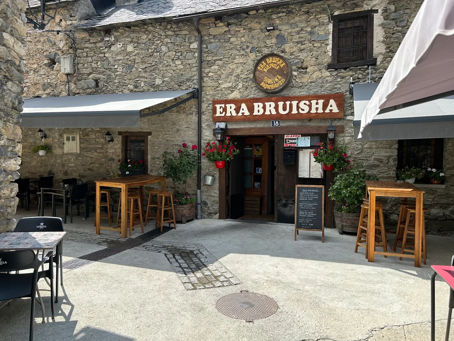 The stone facade and wooden 'ERA BRUISHA' sign of the cider house in Vielha, with pavement tables and hanging flowers