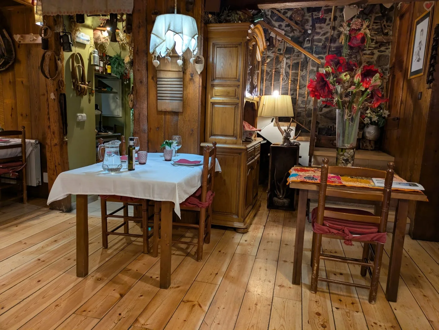 The cosy, antique-filled dining room of Era Caseta des deth Mestre in Tredòs, with a table set beneath a lace lampshade on a wooden floor
