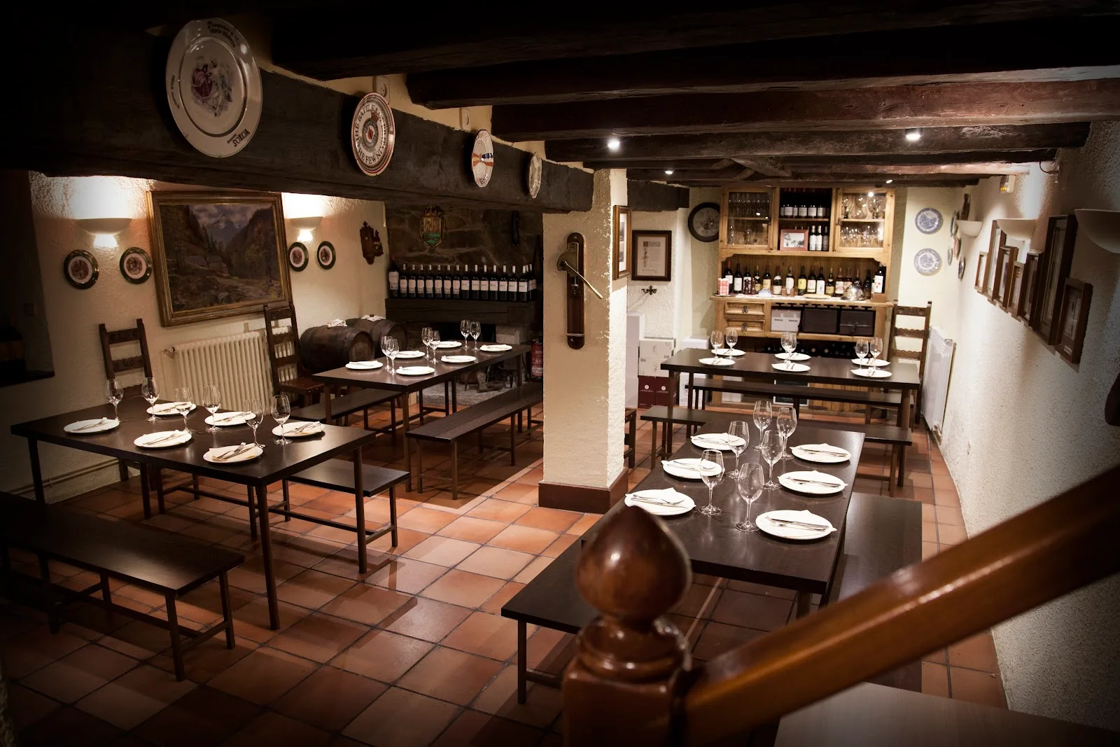 The warm, wood-beamed dining room of Eth Cornèr in Vielha, with wine on a rustic dresser and tables laid on a terracotta-tiled floor